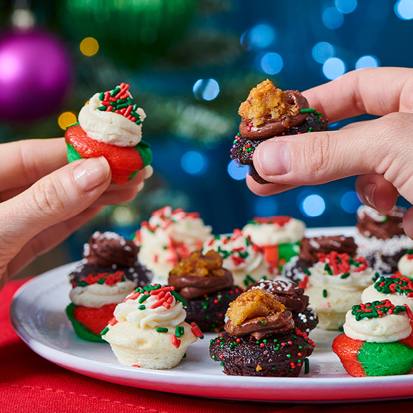 plate of holiday bite-size cupcakes, two are held above in a cheers